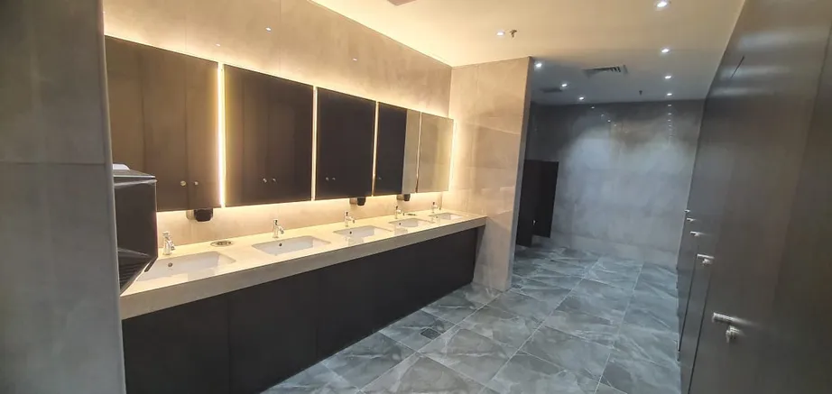 Refurbished public washroom at Senai Airport with backlit mirrors, stone tiling and dark timber vanity